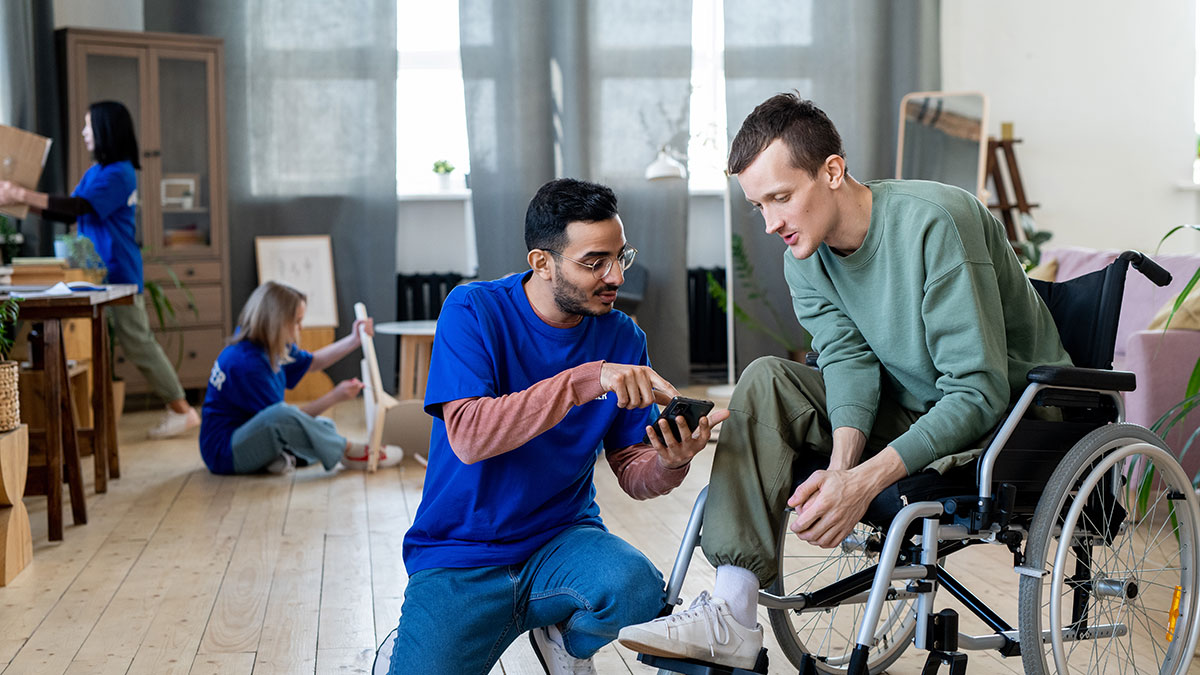 A person with a visible disability in their home, engaging with a service provider while others work in the background.