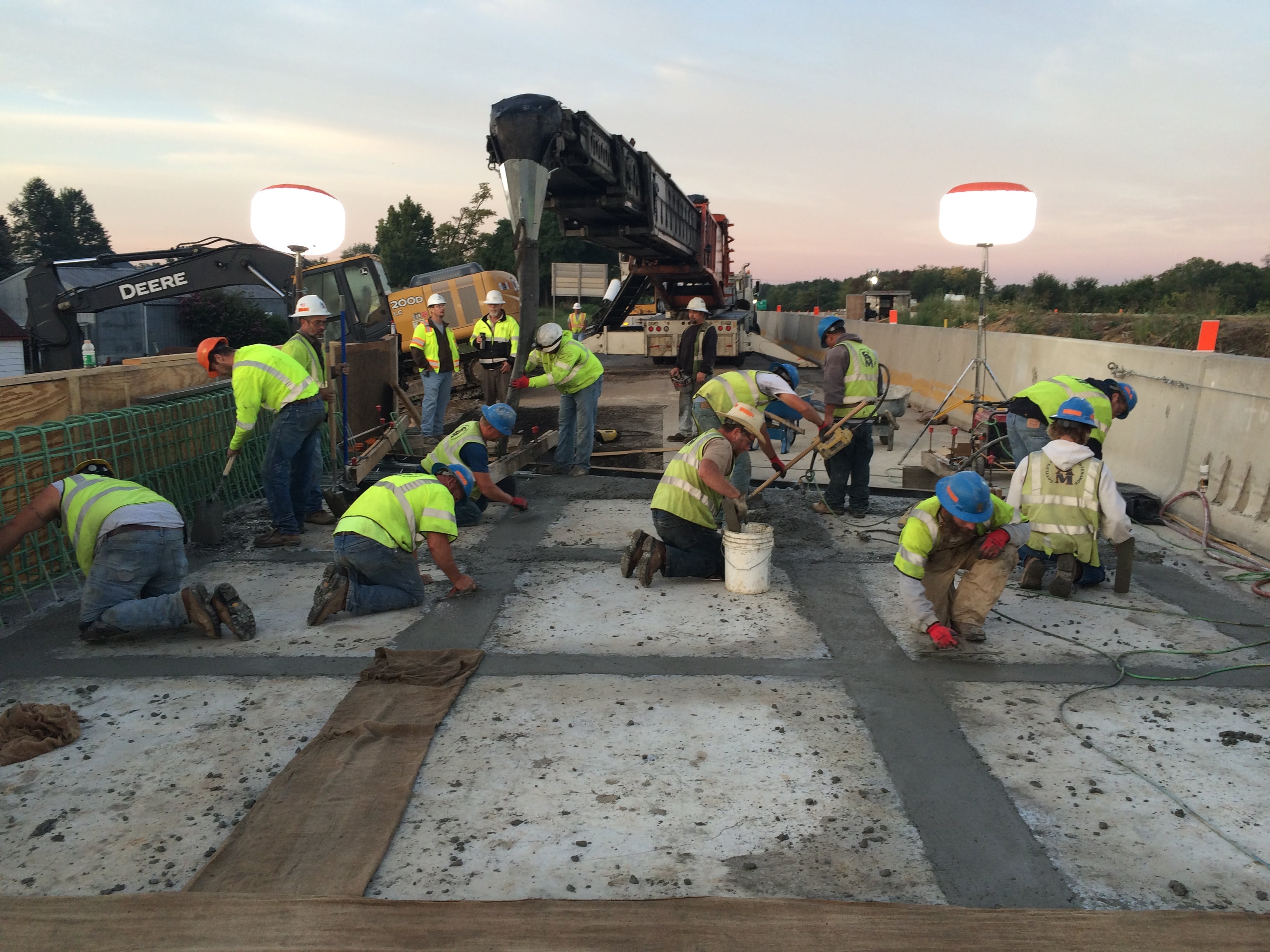 An image of construction workers in hard hats and yellow safety vests applying Ultra-High Performance Concrete between prefabricated bridge elements