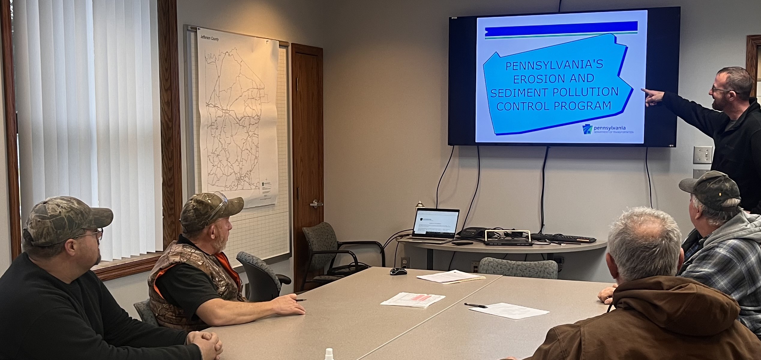 Employees in a conference room listening to a presentation and viewing information on the screen at the front of the room