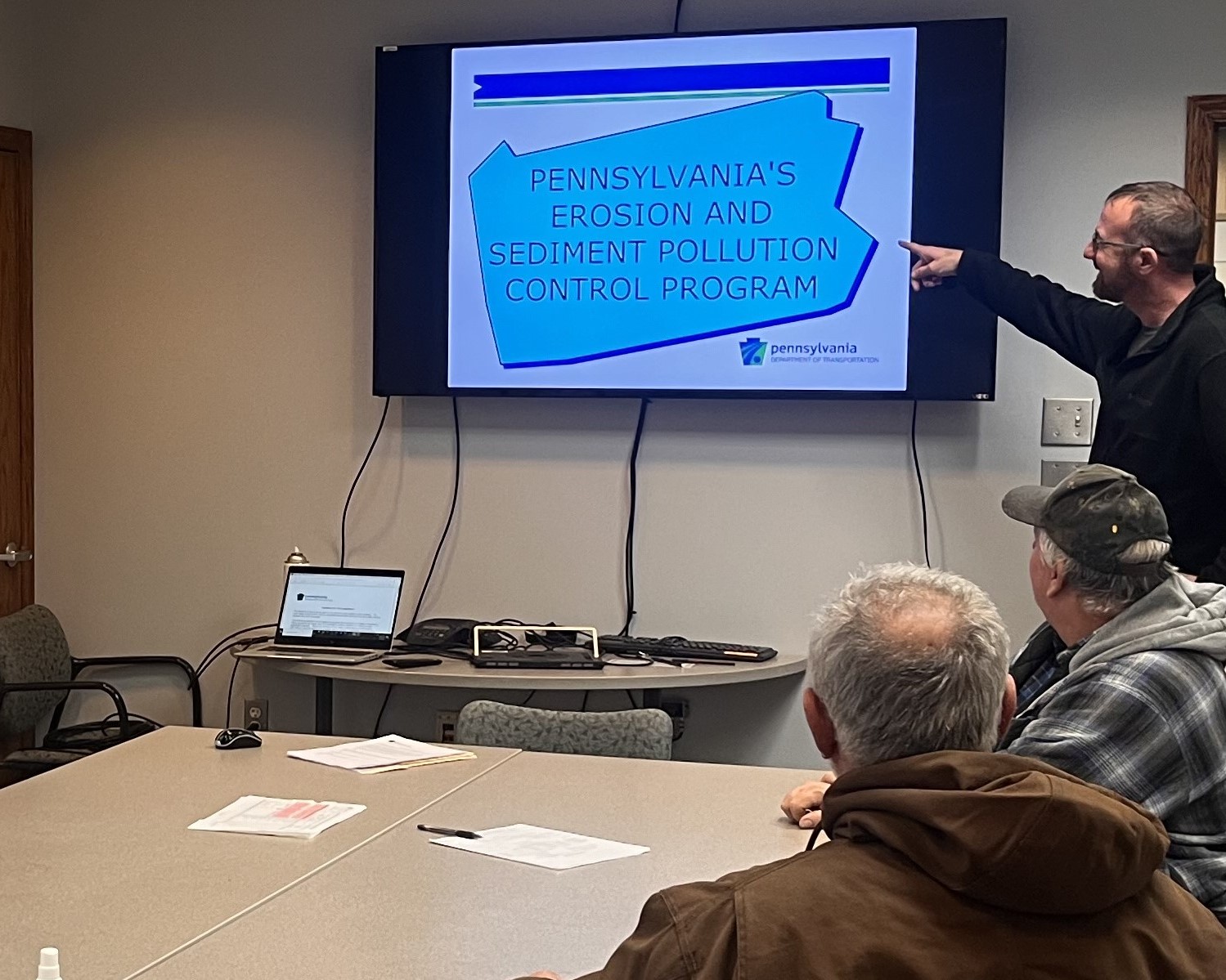 Employees in a conference room listening to a presentation and viewing information on the screen at the front of the room